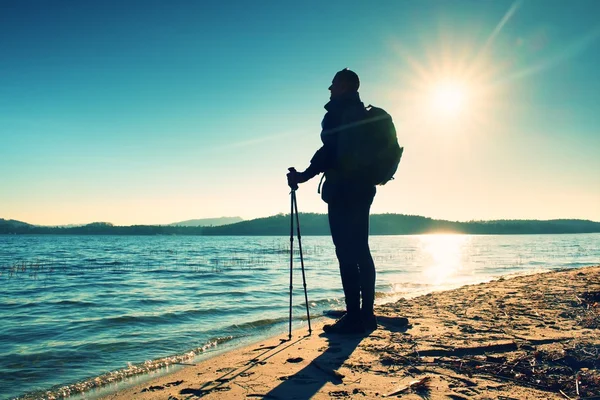 Hiker in dark sportswear with poles and sporty backpack on beach enjoy sunny day. — Stock Photo, Image