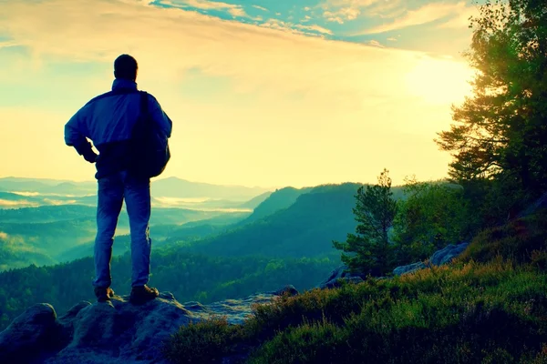 Silueta de turista con mochila. Amanecer soleado de primavera en montañas rocosas. Caminante con mochila deportiva de pie en el punto de vista rocoso por encima del valle brumoso . — Foto de Stock