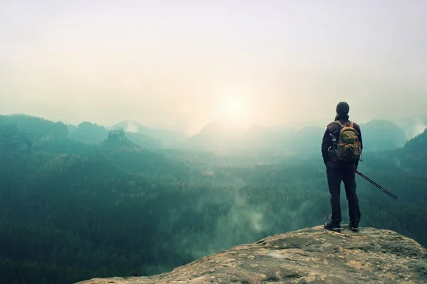 Турист з рюкзаком і стовпами на скелі і спостерігаючи в глибокому туманній долині. Сонячний весняний день у горах . — стокове фото