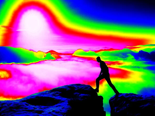 Man op rotsachtige piek. Fantastische infrarood scan. Zware mist in diepe vallei in kleuren van ultra violet meting — Stockfoto