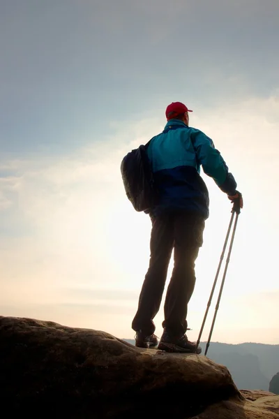Піший турист у вітряній воді, бейсбольна шапка і з пішохідними полюсами стоять на вершині гори . — стокове фото