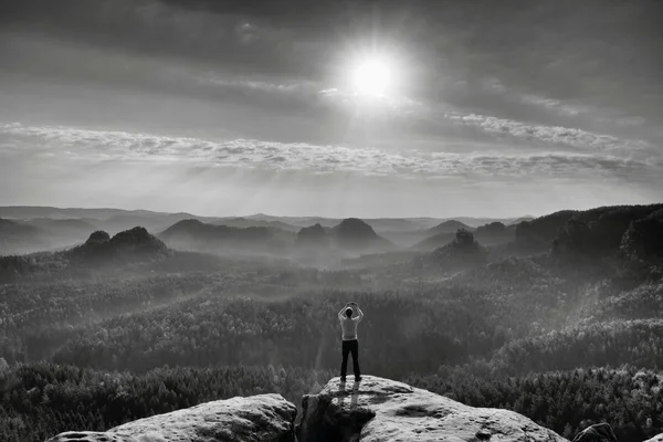 Man takes photos with smart phone on peak of rock empire. Dreamy fogy landscape, spring orange pink misty sunrise in a beautiful valley of Saxony Switzerland park. — Stock Photo, Image