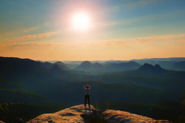 L'uomo scatta foto con smart phone sulla vetta dell'impero rock. Paesaggio nebbioso da sogno, primavera arancio rosa nebbia alba in una splendida valle del parco della Sassonia Svizzera . — Foto Stock