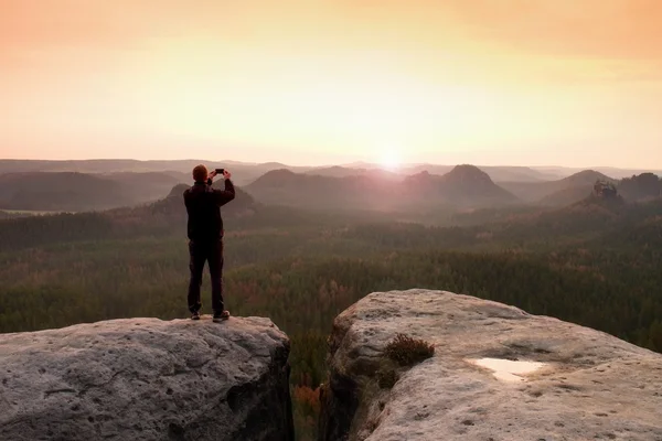 Fotografia de homem com foneof paisagem montanhosa sonhadora, primavera laranja rosa nebuloso nascer do sol em um belo vale — Fotografia de Stock