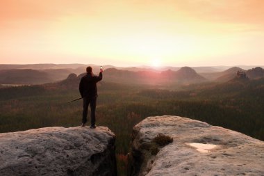 Uzun yürüyüşe çıkan kimse ayağa dağ ve zevk bahar gündoğumu üstüne akıllı telefon ile. Turist Rehberi