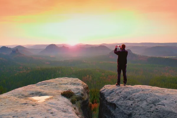 Az ember phoneof álmodozó dombos táj fotózás, tavaszi narancs rózsaszín ködös sunrise, egy gyönyörű völgyben — Stock Fotó