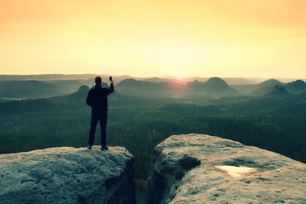 Caminante fotografía amanecer por teléfono inteligente. El hombre se queda en el pico de roca — Foto de Stock