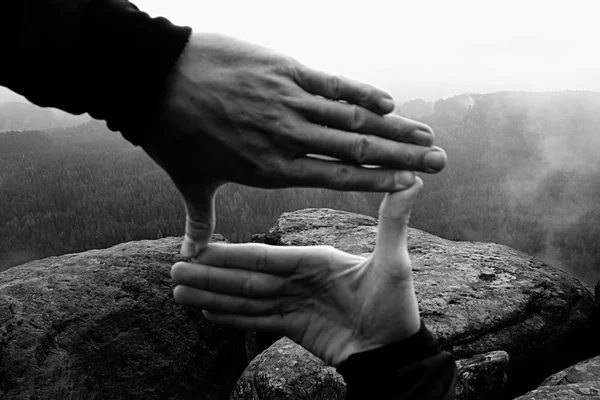 Närbild på händerna gör ram gest. Blå misty valley bellow rocky peak. Regnig vårdag. — Stockfoto