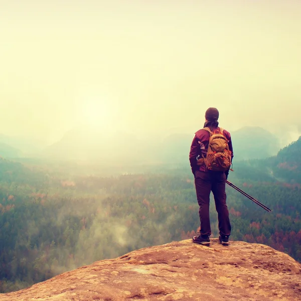 Турист с рюкзаком и палками на скале и наблюдает за глубокой туманной долиной. Солнечный весенний день в горах . — стоковое фото