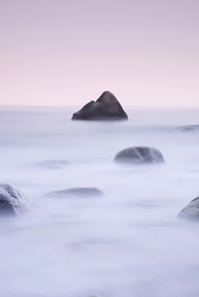 海でロマンチックな朝。大きな岩が滑らかな波状の海から突き出ています。最初の熱い太陽光線とピンク horozon. — ストック写真