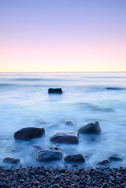 海でロマンチックな朝。大きな岩が滑らかな波状の海から突き出ています。長時間露光 — ストック写真