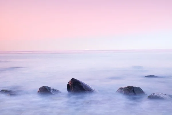 Ambiance romantique dans une matinée paisible en mer. De gros rochers sortent de la mer ondulée et lisse. horizon rose — Photo