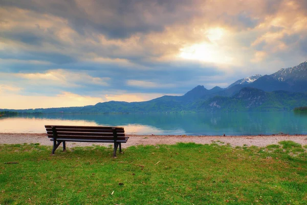 Empty bench at spring montain lake. Coast with mountains at horizon and in water mirror. Vintage toned photo. — Stock Photo, Image