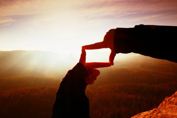 Hände in Großaufnahme, Geste eines Rahmens. orangefarbenes Nebeltal. Sonnenaufgang im Frühling in den Bergen. — Stockfoto