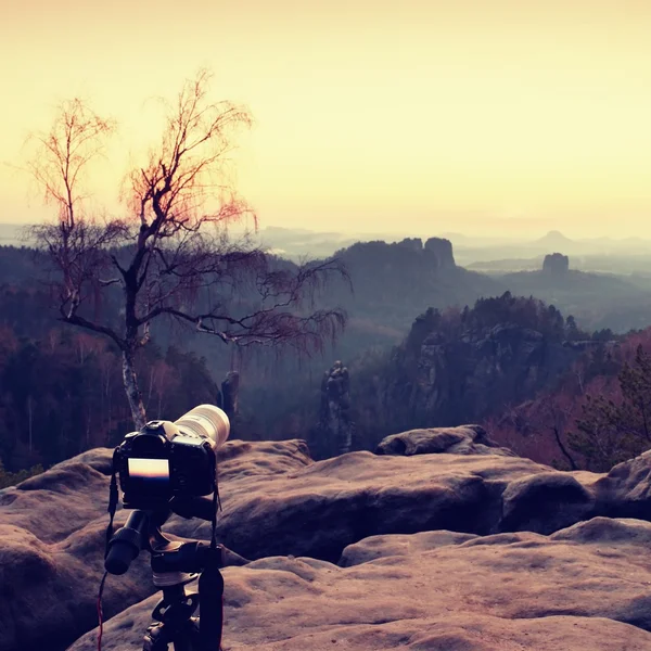 Stativ med stora kameran stå på bergstoppen efter solnedgången. Skarpa sandsten klippor — Stockfoto