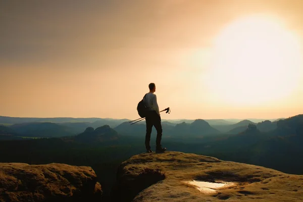 Tall ginger hair hiker in grey t-shirt and dark trekking trousers on cliff. Man with tourist poles in hand and sporty backpack above valley. — Stock Photo, Image