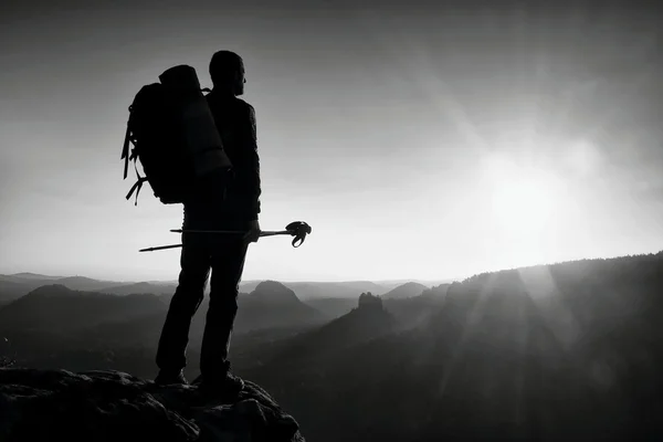 Tall backpacker med stolpar i handen. Soliga vandring dag i Klippiga bergen. Vandrare med stor ryggsäck stå på rocky synvinkel ovan misty valley. — Stockfoto