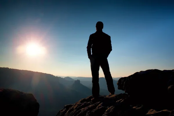 Slim turista sulla vetta tagliente della montagna rocciosa sta vegliando sulla nebbiosa e nebbiosa valle del mattino al sole — Foto Stock