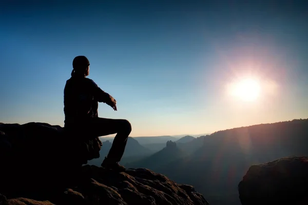 Junger Mann in schwarzer Sportbekleidung sitzt auf Klippe und blickt auf nebliges Tal — Stockfoto