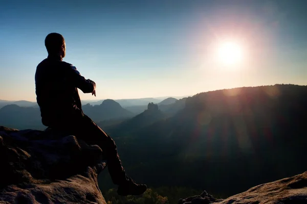 Man tourist sit finally on peak of mountain. Travel mountain scene. Sun at horizon — Stock Photo, Image