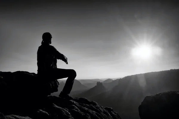 Joven en ropa deportiva negro está sentado en el acantilado y mirando a misty valle abajo —  Fotos de Stock