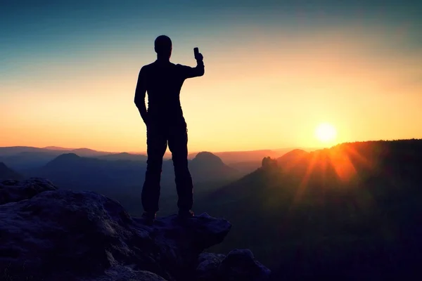 Selfie-Manie. großer Mann Wanderer macht Selfie-Foto mit dem Smartphone auf Gipfel des Berges bei Sonnenaufgang. — Stockfoto