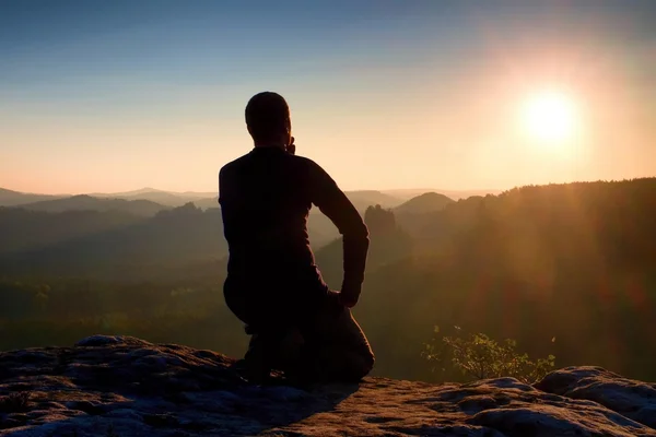 Sportsmann hiker in black sportswear sit on mountain top and take a rest. Tourist  watch down to morning misty valley. — Stock Photo, Image