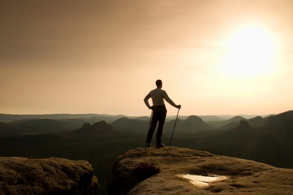 Hombre de pelo jengibre en camiseta gris y pantalones de trekking oscuros sobre roca afilada. Turista con polo sobre valle brumoso . —  Fotos de Stock