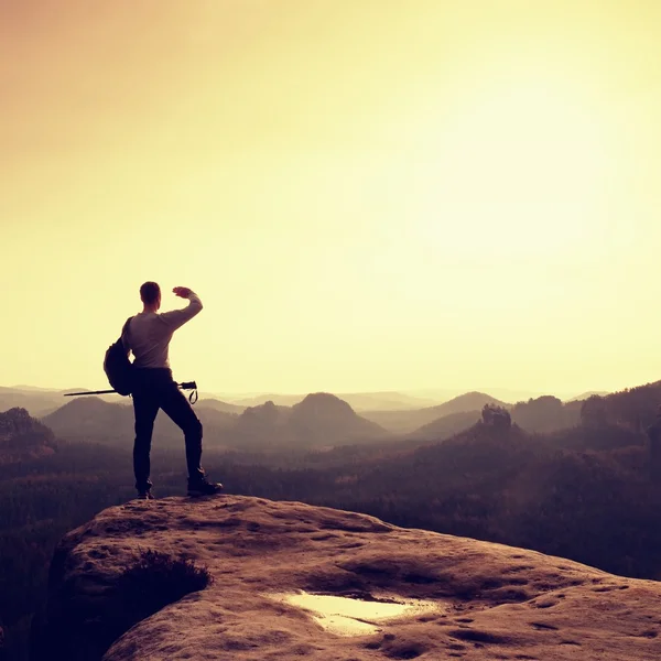 Tall backpacker with poles in hand. Sunny spring daybreak in rocky mountains. Hiker with big backpack stand on rocky view point above misty valley. — Stock Photo, Image