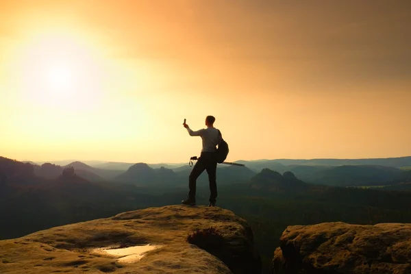 Großer Backpacker mit Stöcken in der Hand. sonniger Frühlingsanbruch in den felsigen Bergen. Wanderer mit großem Rucksack stehen auf felsigem Aussichtspunkt über nebligem Tal. — Stockfoto