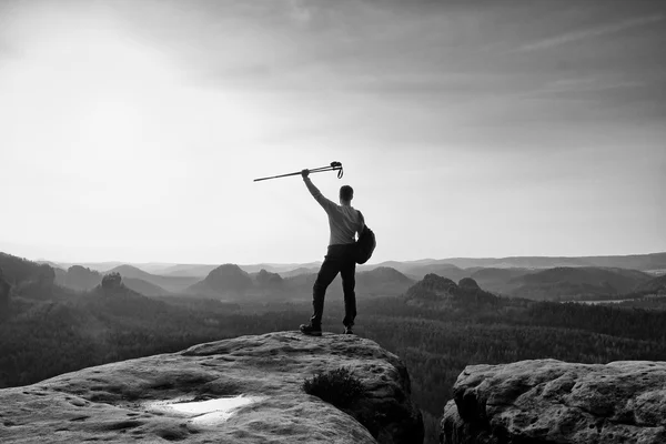 Tall backpacker med stolpar i handen. Soliga våren gryning i Klippiga bergen. Vandrare med stor ryggsäck stå på rocky synvinkel ovan misty valley. — Stockfoto