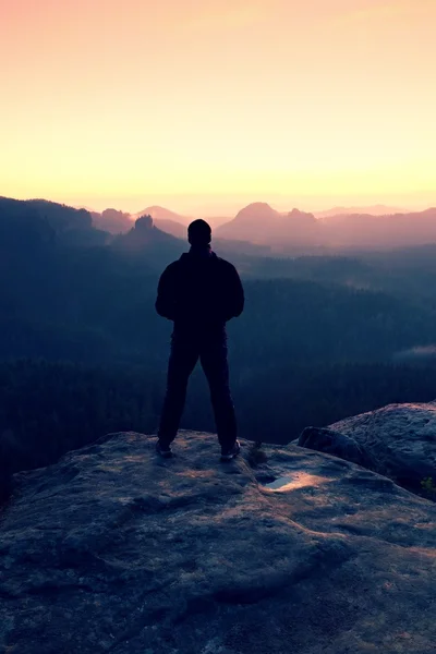 Hombre alto en negro en el acantilado y ver a la salida del sol de la montaña.Silhouette en pose segura de sí mismo — Foto de Stock
