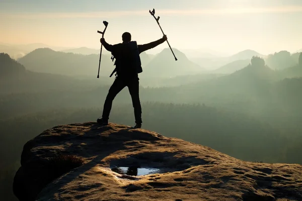 Hiker with broken leg in immobilizer. Tourist with  medicine crutch above head achieved mountain peak. — Stock Photo, Image