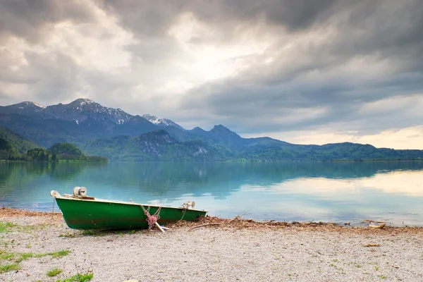 Abandoned fishing paddle boat on bank of Alps lake. Morning lake glowing by sunlight. — Stock Photo, Image