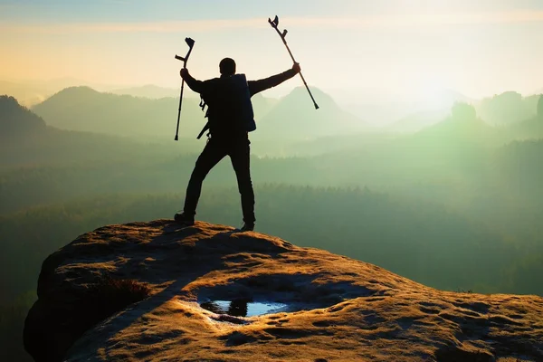 Tourist with  medicine crutch above head achieved mountain peak. Hiker with broken leg in immobilizer. — Stock Photo, Image