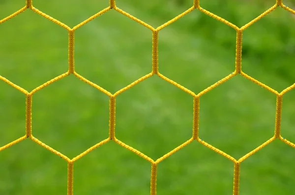 Detail of yellow blue crossed soccer nets, soccer football in goal net with grass on playground in background. Honeycomb shape. — Stock Photo, Image