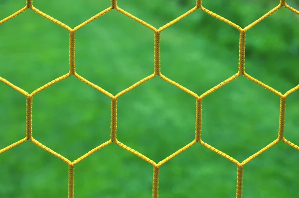 Detail of yellow blue crossed soccer nets, soccer football in goal net with grass on playground in background. Honeycomb shape. — Stock Photo, Image