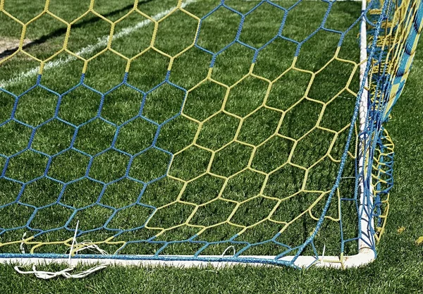 Detail von gelb blau gekreuzten Fußballnetzen, Fußball im Tornetz mit Rasen auf dem Spielplatz im Hintergrund. Wabenform. — Stockfoto