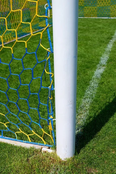 Detail žlutá modrá překročil fotbalové sítě, fotbal fotbal v brance čisté s trávou na hřišti v pozadí. Tvar plástev. — Stock fotografie