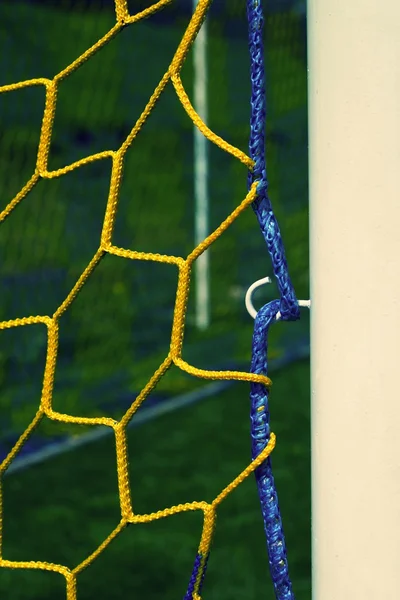 Detalj av gul blå korsade fotboll nät, fotboll fotboll i netto med gräs på lekplatsen i bakgrunden målet. Bikakestruktur form. — Stockfoto