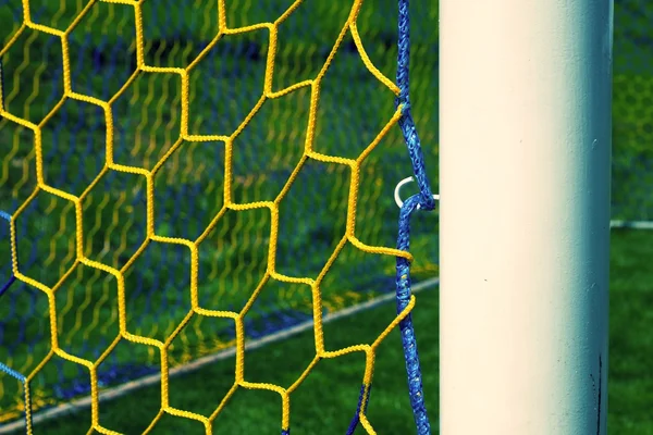Detail žlutá modrá překročil fotbalové sítě, fotbal fotbal v brance čisté s trávou na hřišti v pozadí. Tvar plástev. — Stock fotografie