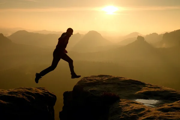 Młody człowiek szalony skok na szczyt góry. Sylwetka skoki człowieka i piękny zachód słońca niebo. Vintage efekt, wady obiektywu. — Zdjęcie stockowe