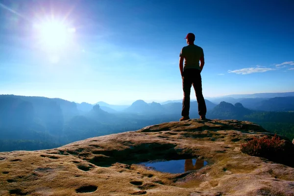 Alone man in red cap on peak of sharp peak in rock empires park and watching over the misty and foggy morning valley to Sun. Beautiful moment — Stock Photo, Image