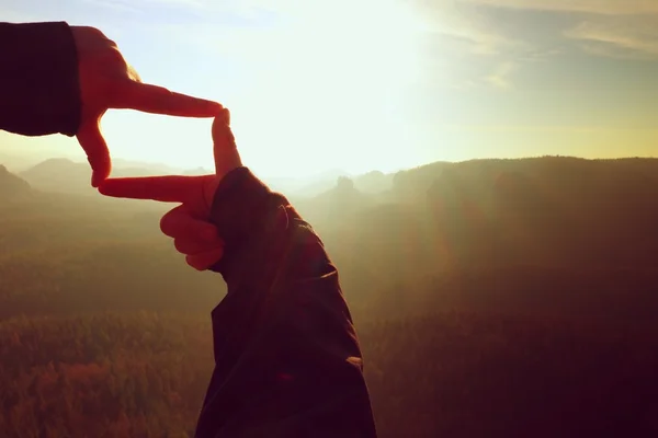 Close up hands making frame gesture. Orange misty valley bellow. Sunny spring daybreak in mountains. — Stock Photo, Image