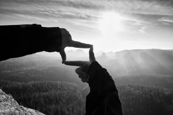 Ženské ruce rámu gesto. Hluboké mlhavé údolí pod sandsotne útesu. Slunečné jarní svítání — Stock fotografie