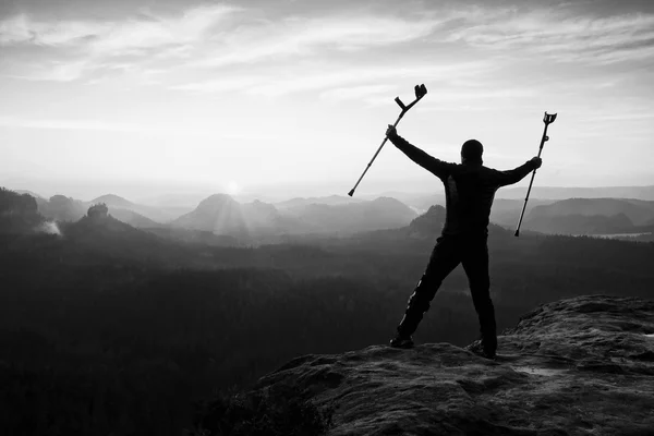 Turista con stampella avambraccio sopra la testa raggiunto vetta di montagna. Escursionista con gamba rotta — Foto Stock