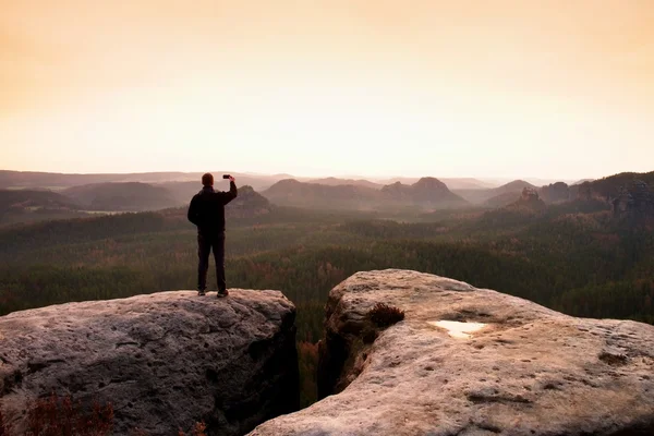 Hiker photography sunrise by smart phone. Man stay on peak of rock — Stock Photo, Image