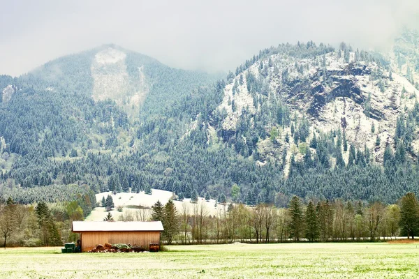 Stodoła z wiejskiej. Wiosna śnieg w górach poniżej łąki. — Zdjęcie stockowe