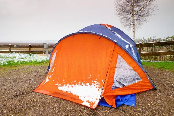 Orange touristic tent with snow. Tent on sand, snowy green grass