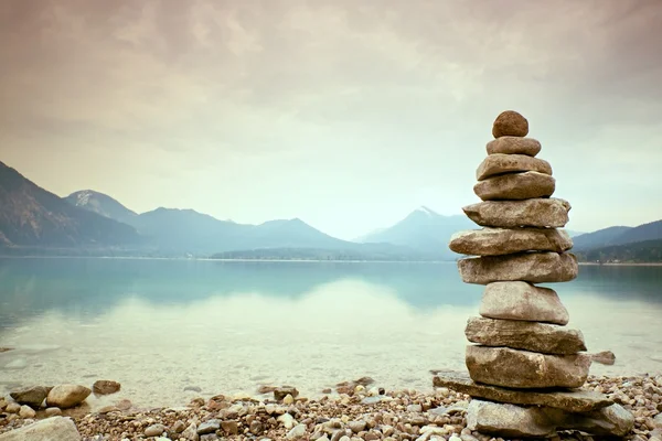 Balanced stone pyramide on shore, blue water of mountain lake.